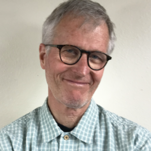 Dwight smiling with glasses and blue and white collared shirt.