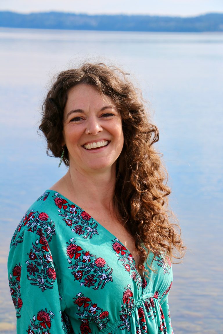 Woman smiling with patterned shirt in front of a body of water.
